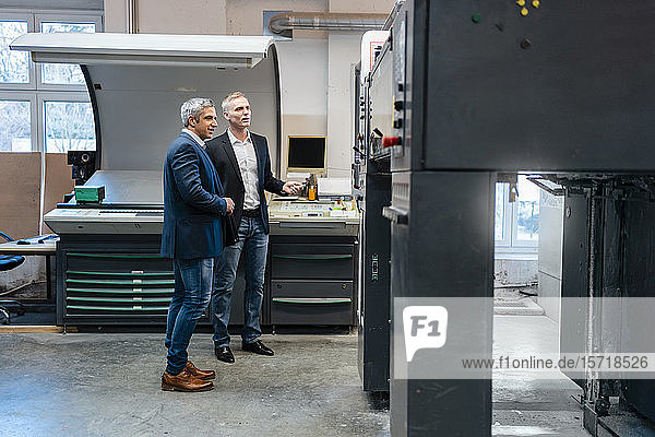 Zwei Geschäftsleute betrachten eine Maschine in einer Fabrik