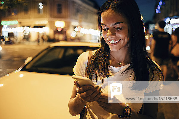 Lächelnde Frau benutzt nachts in der Stadt ein Smartphone