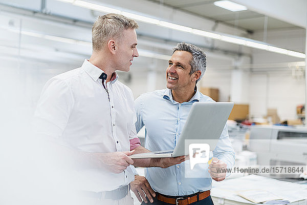 Zwei Kollegen diskutieren mit Laptop in einer Fabrik
