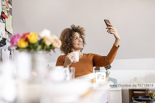 Frau hält Kaffeetasse und nimmt sich zu Hause ein Selfie