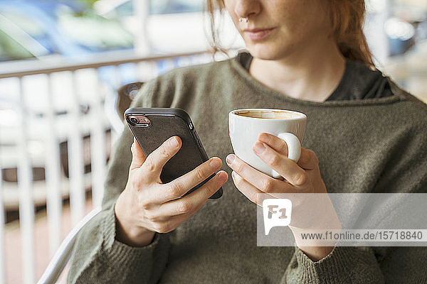 Nahaufnahme einer jungen Frau  die ein Mobiltelefon benutzt und eine Kaffeetasse hält