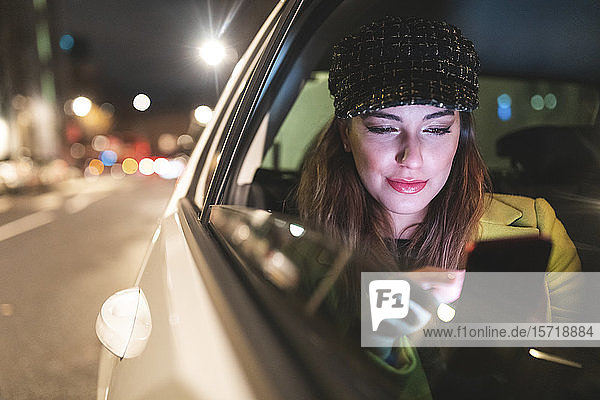 Woman sitting on the backseat of a car in the city at night