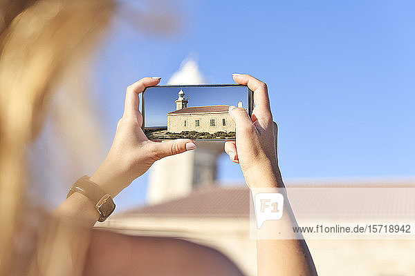 Young woman taking pictures of Punta Nati lighthouse  Menorca  Spain
