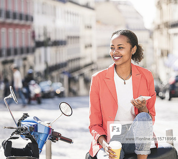 Lächelnde junge Frau mit Motorroller und Handy in der Stadt  Lissabon  Portugal