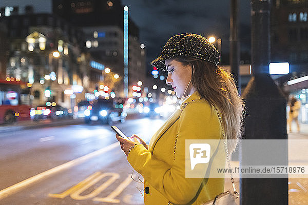 Woman with her smartphone in the city at night next to a road in London  Great Britain