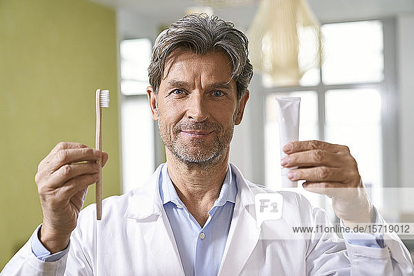 Porträt eines Zahnarztes mit Zahnbürste und Zahnpasta in seiner Praxis
