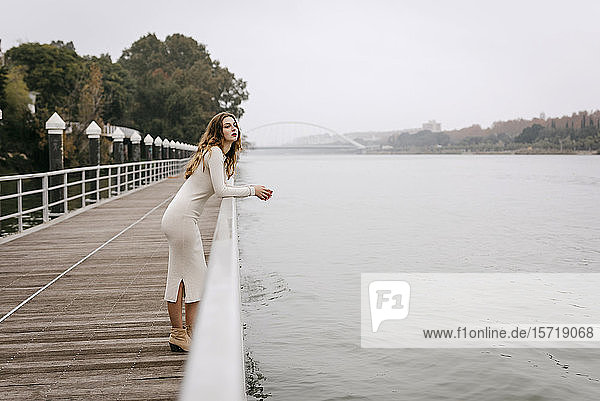 Porträt einer jungen Frau in weißem Kleid  die sich an einem Regentag an ein Geländer lehnt