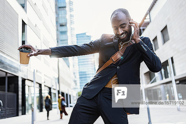 Porträt eines glücklichen jungen Geschäftsmannes  der auf der Straße tanzt  während er mit Kopfhörern Musik hört