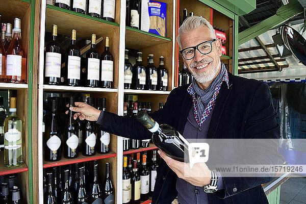 Porträt eines lächelnden reifen Mannes bei der Auswahl einer Flasche Wein in einem Weinladen