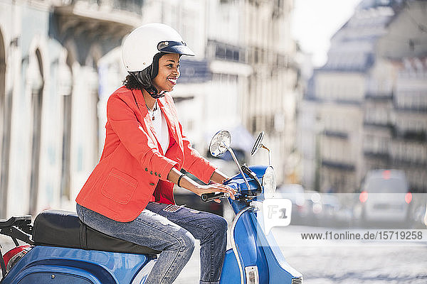 Lächelnde junge Frau fährt Motorroller in der Stadt  Lissabon  Portugal