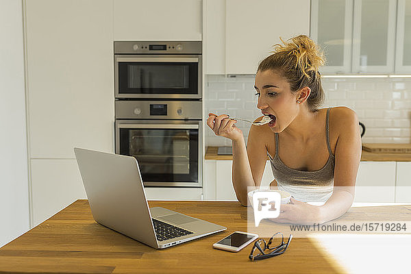 Weiblicher Teenager benutzt Laptop während des Frühstücks in der Küche