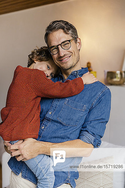 Porträt eines lächelnden Vaters  der seine Tochter zu Hause trägt