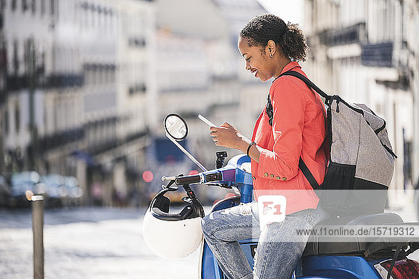 Junge Frau benutzt Handy auf Motorroller in der Stadt  Lissabon  Portugal
