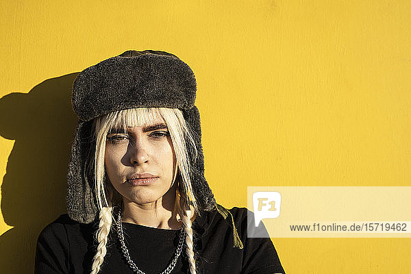 Bildnis einer jungen Frau mit blonden Zöpfen  die eine Mütze gegen eine gelbe Wand trägt