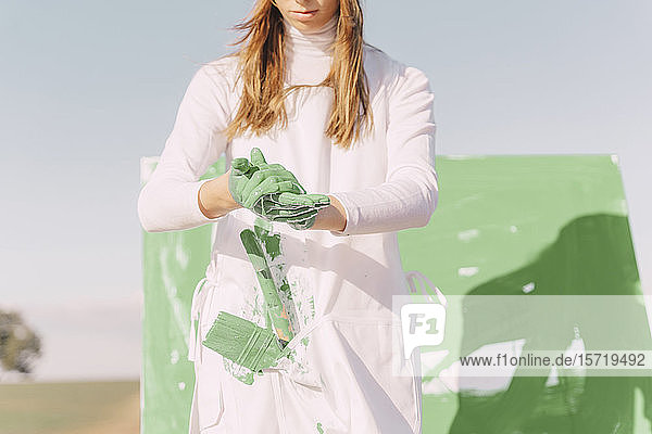 Young woman on dry field  painting canvas with green paint