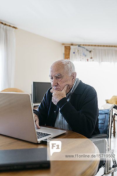 Portrait of senior man in wheelchair using laptop at home