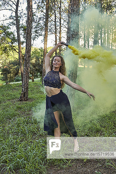 Porträt einer jungen Frau  die mit gelbem Rauch im Wald tanzt