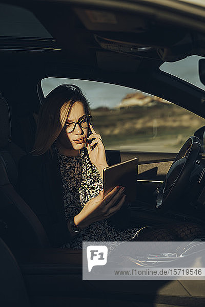 Junge blonde Frau mit Smartphone und Tablet im Auto