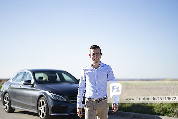 Portrait of smiling young businessman with car on country road