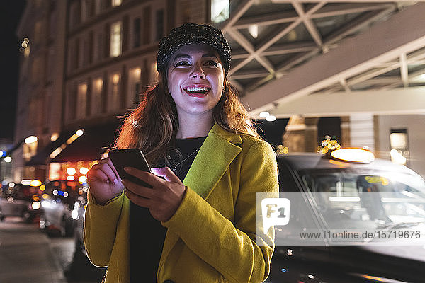 Frau  die nachts in der Stadt auf ihrem Smartphone tippt und lächelt
