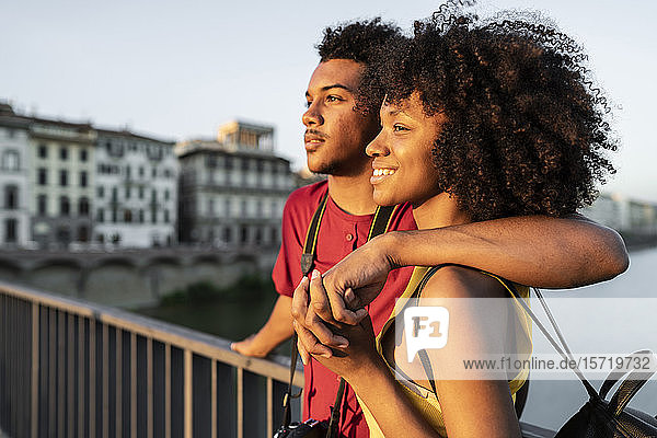 Happy young tourist couple on a bridge above river Arno at sunset  Florence  Italy