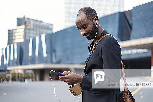 Porträt eines lächelnden jungen Geschäftsmannes mit Kaffee zum Musikhören mit Kopfhörern und Smartphone