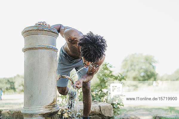 Junger Mann beim Training  trinkt aus Brunnen in einem Park