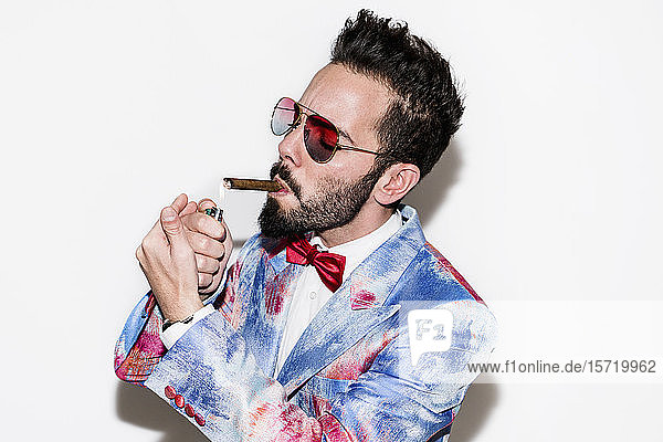 Cool and stylish man wearing a colorful suit and sunglasses lighting a cigar