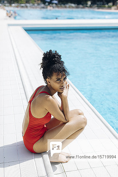 Porträt einer jungen Frau im roten Badeanzug am Poolufer sitzend