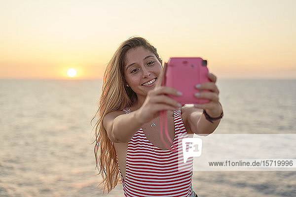 Junge Frau fotografiert sich bei Sonnenuntergang am Meer