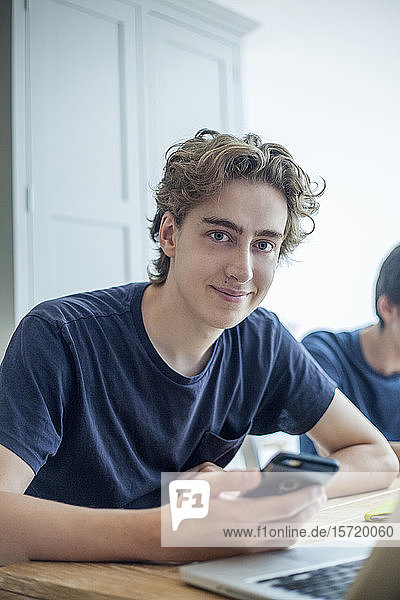 Portrait of smiling teenage boy with smartphone and laptop at home