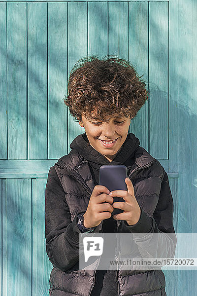 Lächelnder Junge benutzt Mobiltelefon im Freien