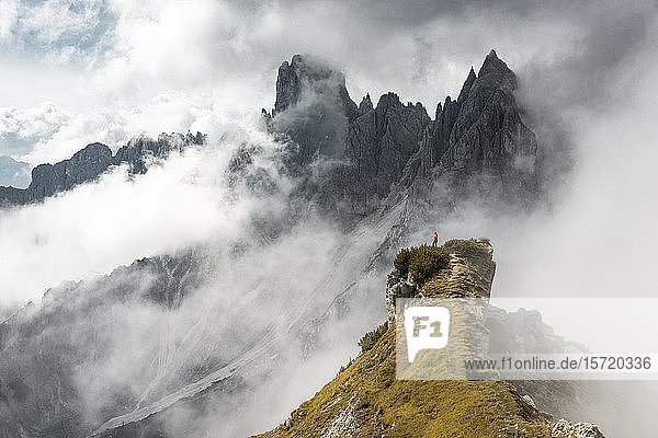 Frau in roter Jacke auf einem Bergrücken stehend  hinter Bergspitzen und spitzen Felsen  dramatische Wolken  Cimon di Croda Liscia und Cadini-Gruppe  Auronzo di Cadore  Belluno  Italien  Europa