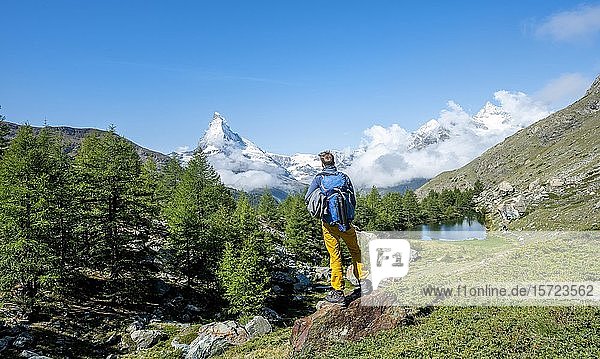 Wanderer steht auf Felsen und schaut in die Ferne  hinter dem Grindij-See und dem schneebedeckten Matterhorn  Wallis  Schweiz  Europa