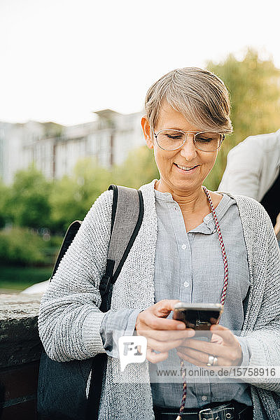 Smiling mature female using phone while standing in city