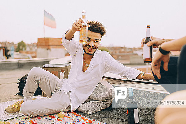 Smiling young man enjoying beer with friend on terrace at rooftop party