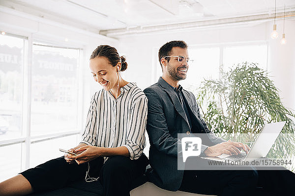 Smiling business coworkers using smart phone and laptop at creative office