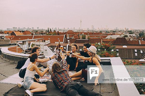Cheerful friends toasting beer while relaxing on terrace at city