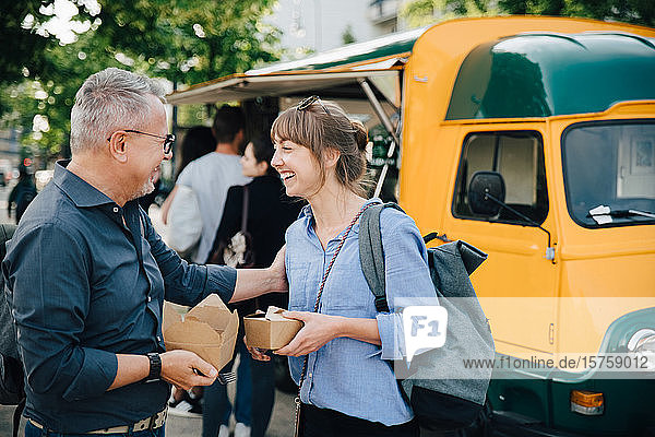 Happy male and female friends talking while standing with food box against commercial land vehicle