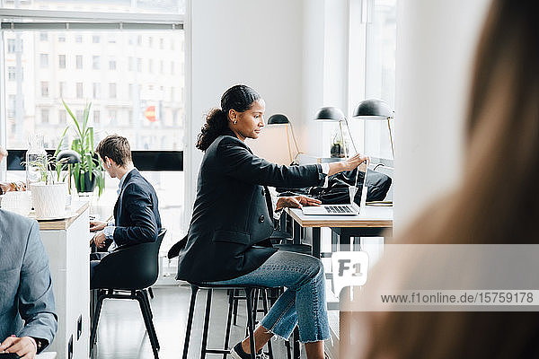 Seitenansicht einer Geschäftsfrau  die am Laptop arbeitet  während sie am Schreibtisch im Bürocafé sitzt