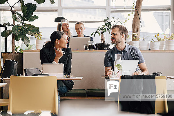 Male and female colleagues discussing while working at desk in coworking space