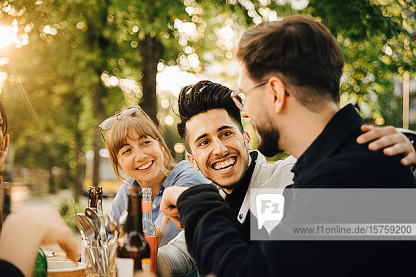 Happy young man sitting by male and female friend at social gathering