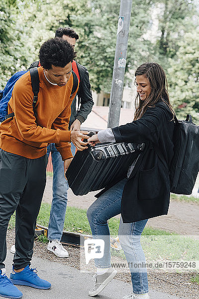 Ein junger Mann in voller Länge hilft einer Freundin mit Gepäck  während er auf der Straße steht