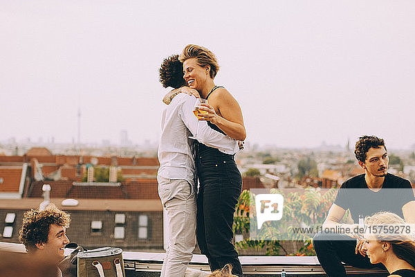 Mann und Frau umarmen sich und feiern mit Freunden auf der Terrasse