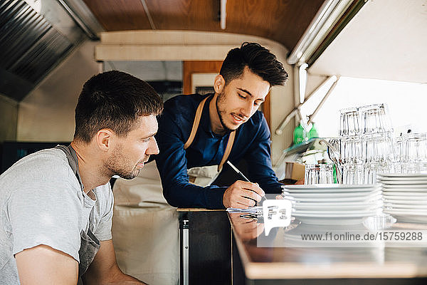 Male coworkers looking at order in food truck