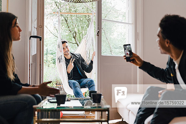 Mann fotografiert Freund mit Smartphone  während er zu Hause in der Schaukel sitzt