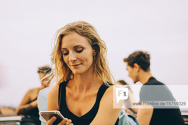 Lächelnde Frau benutzt Mobiltelefon während einer Dachfeier