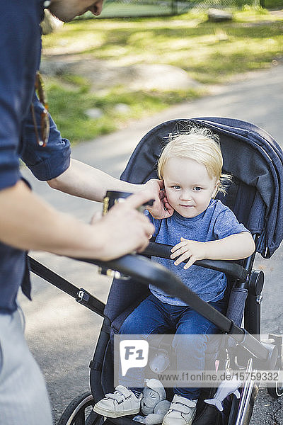 Midsection of man touching son sitting on baby carriage at public park