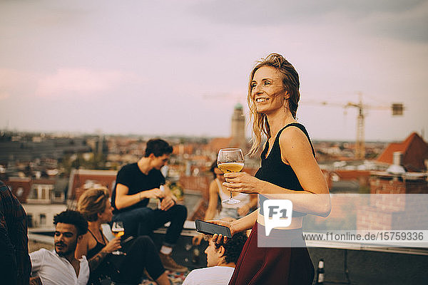 Lächelnde Frau genießt Getränk während einer Party mit Freunden auf dem Dach