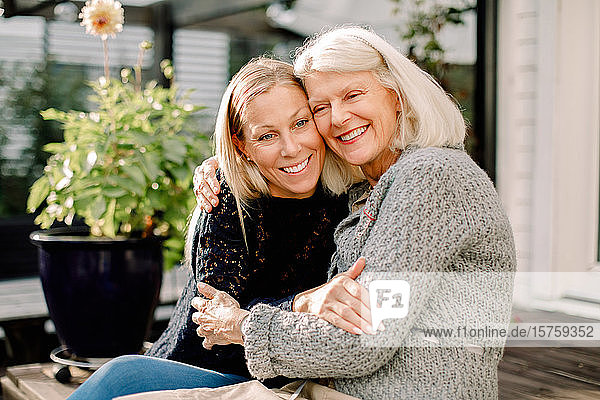 Smiling mother and daughter with arm around sitting in backyard